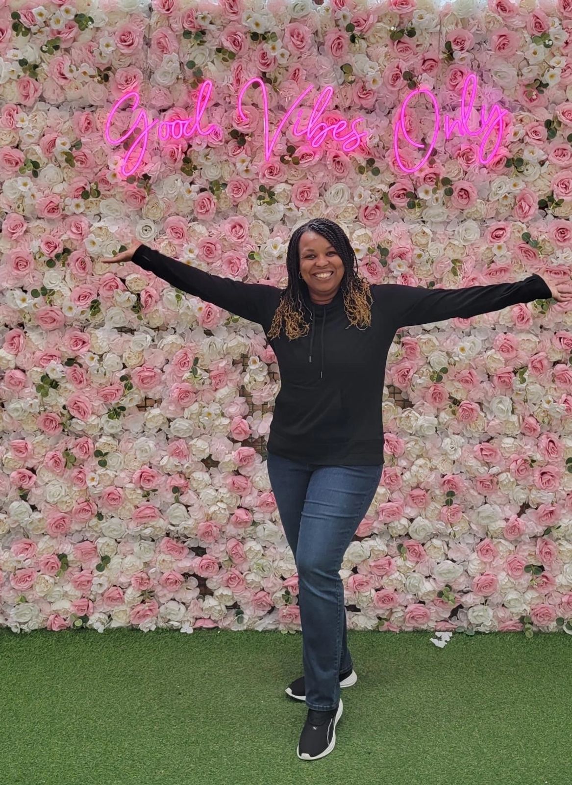 Unique Porter, Owner and Lead Travel Advisor of Unique World Travel LLC, standing with her arms outstretched in front of a pink and white flower wall